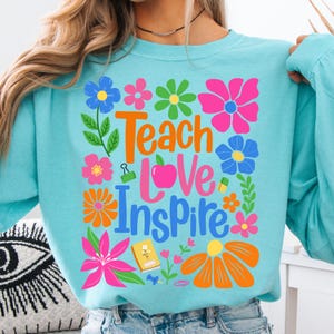 May include: A light blue long-sleeved shirt with a colorful floral design and the text "Teach Love Inspire".