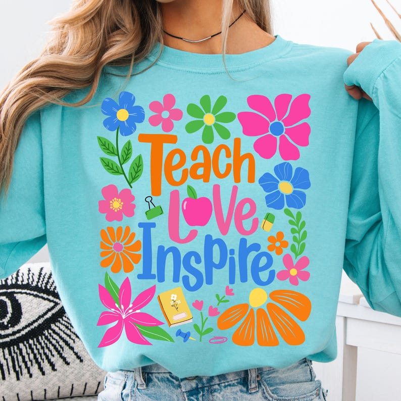 May include: A light blue long-sleeved shirt with a colorful floral design and the text "Teach Love Inspire".