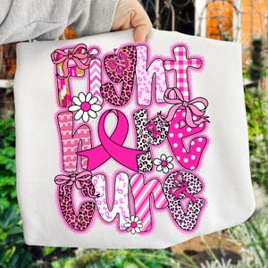 以下が含まれることがあります： ピンク色の「FIGHT HOPE CURE」という言葉が書かれた白いトートバッグ。さまざまなパターンとデザインが施されています。デザインには、ピンクのリボン、リボン、花、十字架が含まれており、乳がんの啓発を支援しています。