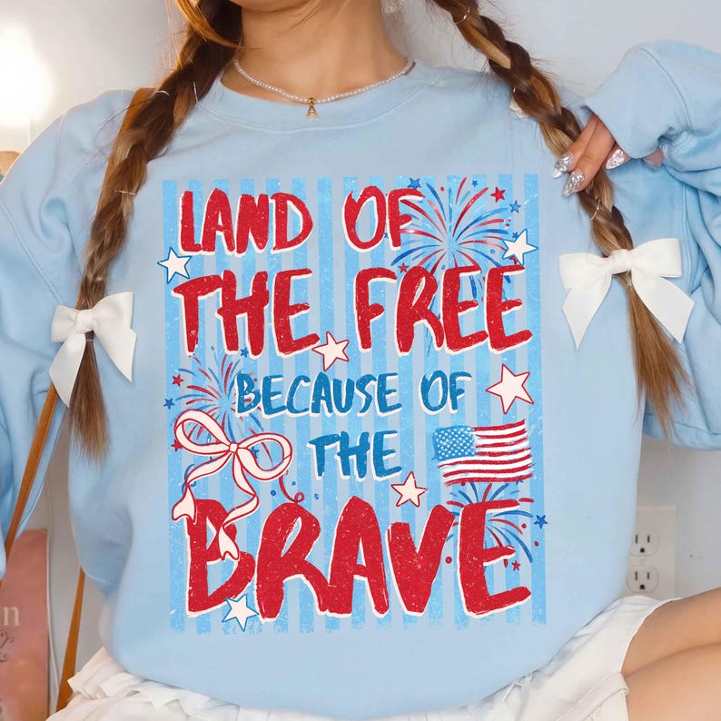 以下が含まれることがあります： 赤と白で「LAND OF THE FREE BECAUSE OF THE BRAVE」の文字が入った水色のスウェットシャツ。花火、星、アメリカ国旗のデザイン。スウェットシャツはクルーネックです。
