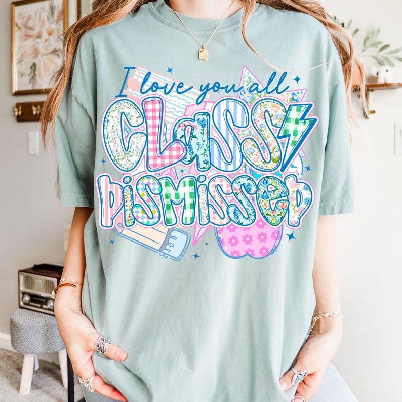 May include: A light blue t-shirt with the text "I love you all Classy Dismissed" in a colorful patchwork design. The text is surrounded by a pencil, a star, and an apple.