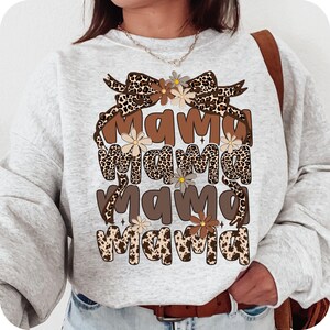 May include: A gray sweatshirt with a brown and black leopard print design. The design features the word "mama" repeated four times with a brown bow and flowers.
