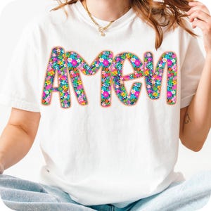 May include: White t-shirt with the word "AMEN" printed in large, colorful letters. The letters are filled with a floral pattern in shades of pink, blue, green, and yellow.