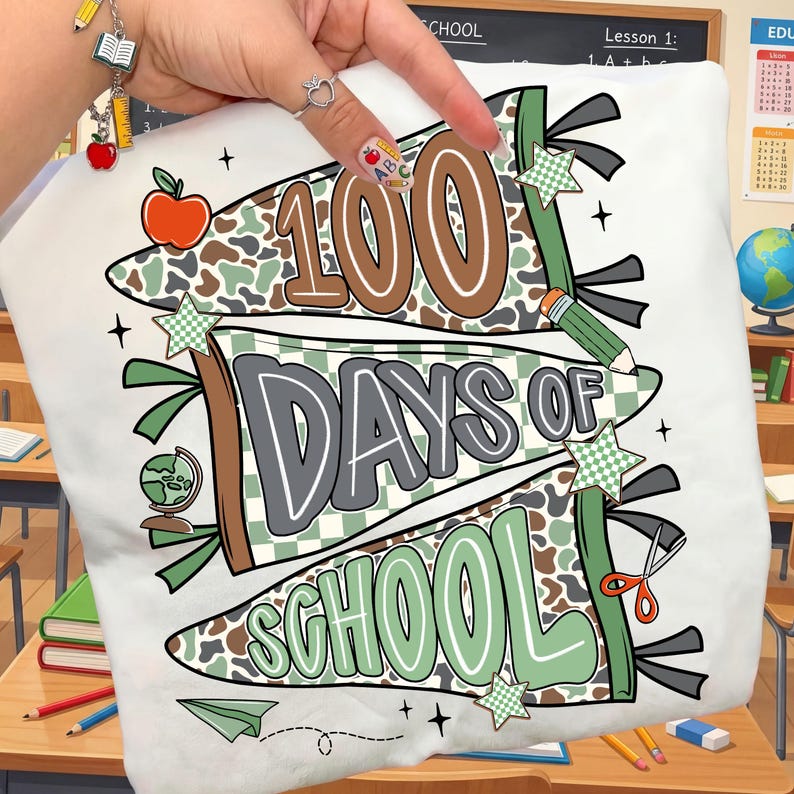 May include: White t-shirt with a colorful graphic celebrating "100 Days of School." The design features banners with the text, along with an apple, pencil, globe, scissors, and stars. The color palette includes brown, green, and gray.
