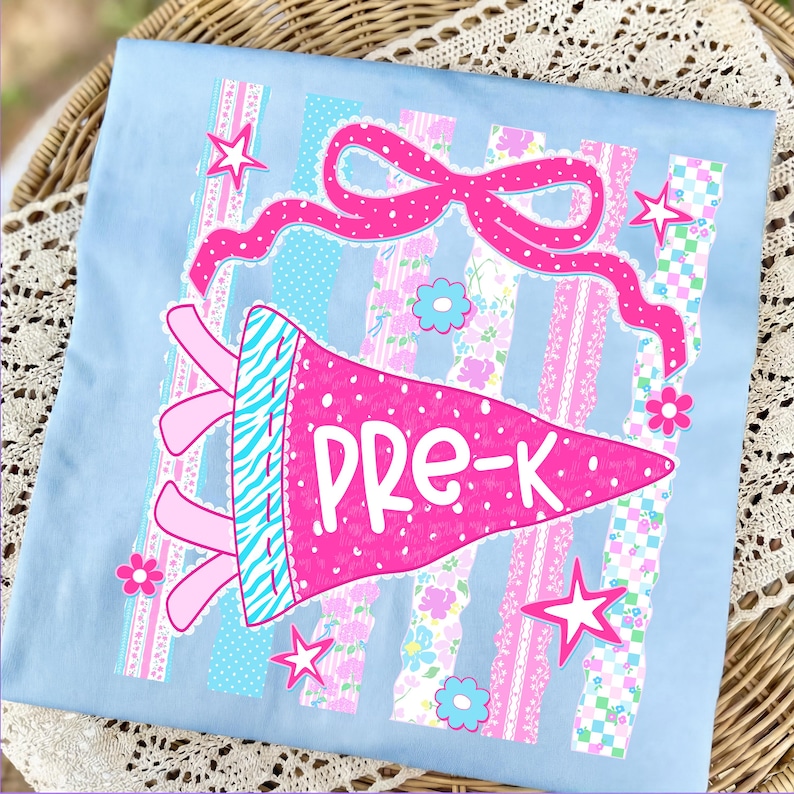 May include: Light blue t-shirt with a pink pennant that says "PRE-K". The pennant has a zebra print and is decorated with a pink bow, stars, and flowers. The background has vertical stripes in various patterns.