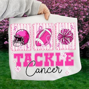 May include: White fabric with pink graphics of a football helmet, football, and pom-pom, each with a pink ribbon. The words "TACKLE Cancer" are in pink, with a black cursive "Cancer" below. The design is on a white background.