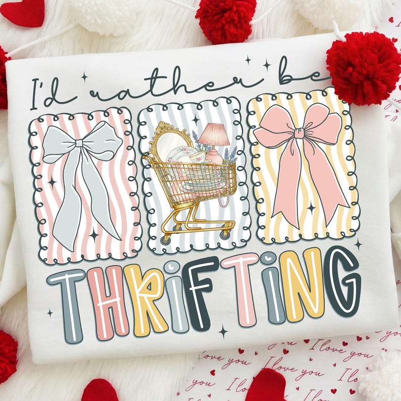May include: White sweatshirt with a colorful graphic that says "I'd rather be THRIFTING." The graphic includes three framed images of a bow, a shopping cart filled with items, and another bow. The text is in a playful font.