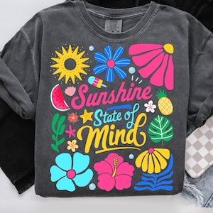 May include: A grey t-shirt with a colourful graphic design featuring flowers, a pineapple, a watermelon, a popsicle, and a sun. The text "Sunshine State of Mind" is written in a yellow, orange, and pink font.