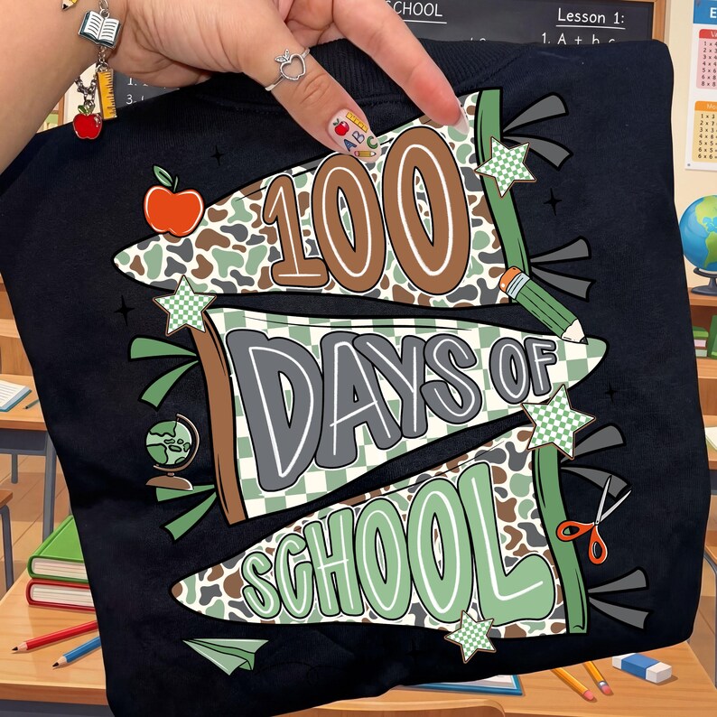 May include: Black sweatshirt with a colorful graphic celebrating 100 days of school. The design includes the text "100 Days of School" in brown, gray, and green, along with school-themed illustrations like an apple, pencil, globe, and scissors.