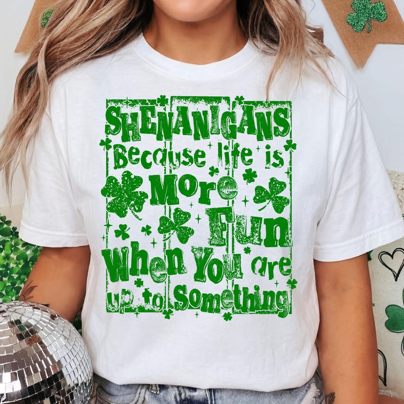 May include: White t-shirt with a green graphic that reads "SHENANIGANS Because life is MORE Fun When You are up to Something." The design includes shamrocks and decorative elements, perfect for St. Patrick's Day.
