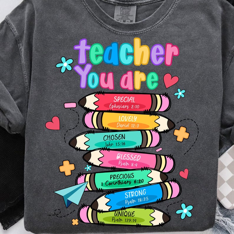 May include: Dark gray sweatshirt with the words "teacher You are" in colorful letters. Below are stacked pencils with words like "SPECIAL", "LOVELY", and "CHOSEN". The sweatshirt has a crew neck and long sleeves. Floral and heart graphics are scattered around the design.