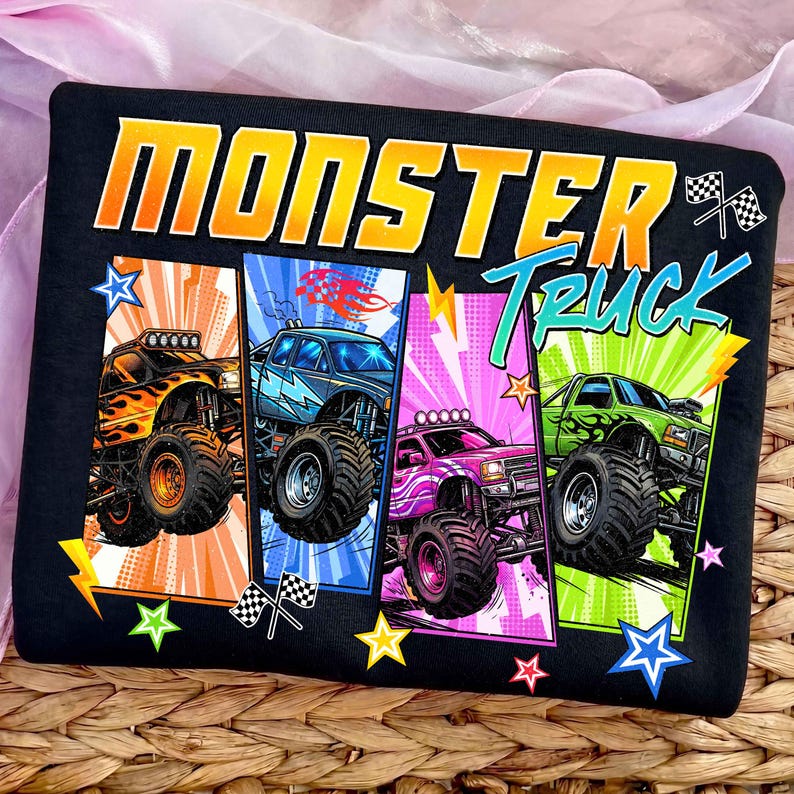 May include: Black t-shirt featuring the words "MONSTER TRUCK" in orange and teal. The shirt displays four colorful monster truck designs with flames, lightning bolts, and stars. Each truck is a different color: orange, blue, pink, and green.