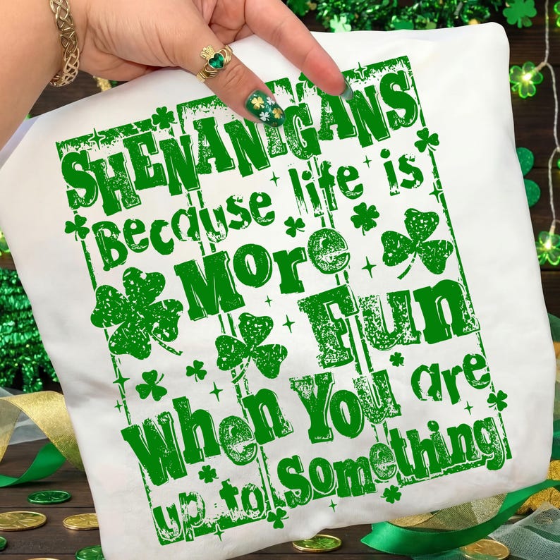 May include: White t-shirt with green text that reads "SHENANIGANS Because life is More FUN When You are up to Something." The design includes shamrocks and decorative elements, perfect for St. Patrick's Day.