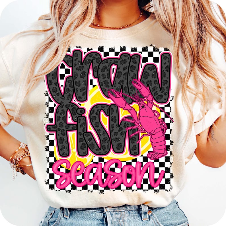 May include: A white t-shirt with a black and white checkered background. The text "Crawfish Season" is written in black with a leopard print pattern. A pink crawfish is on top of a yellow lemon.