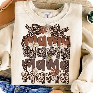 May include: A cream-colored sweatshirt with the text "mama mama mama mama" in brown letters with a leopard print background. The text is surrounded by a brown bow with a leopard print and small brown and white flowers.