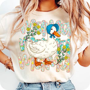 May include: Cream-coloured sweatshirt with a cartoon duck wearing a blue bonnet and floral accents. The word "MOM" is repeated in a floral pattern. Yellow flowers and green stems are also present.