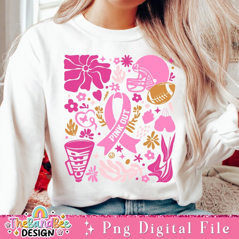 May include: A white sweatshirt with a pink and gold design featuring a pink ribbon, a football helmet, a football, and flowers. The ribbon has the text "Pink Out" on it.