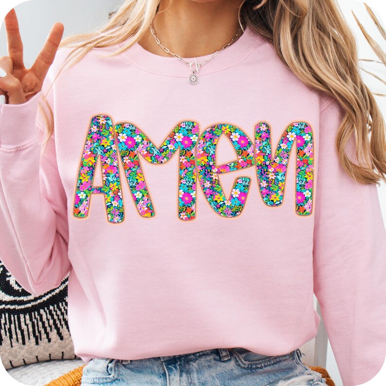 May include: Pink sweatshirt with the word "AMEN" in large, colorful letters made of floral patterns.