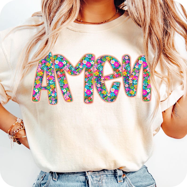 May include: A white t-shirt with the word "Amen" printed in large, colorful letters. The letters are filled with a floral pattern in shades of pink, blue, yellow, and green.