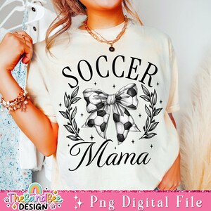 May include: A white t-shirt with black text that reads "Soccer Mama". The text is surrounded by a wreath of leaves and a black and white soccer ball bow.
