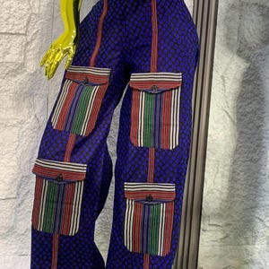 May include: Blue patterned pants with vertical red stripes and striped pockets. The pockets feature red, green, and white stripes. The pants are part of a matching set.
