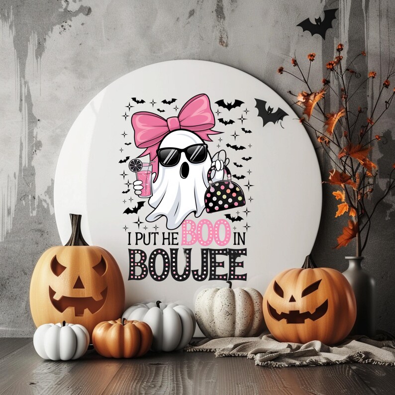 May include: A white ghost with pink hair and sunglasses holding a pink drink and a black and white purse. The ghost is surrounded by bats and stars. The text "I put the BOO in BOUJEE" is below the ghost.
