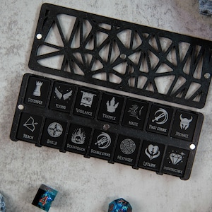 May include: Black and white dice with various symbols, including a shield, a sword, and a skull, are arranged in a black tray with a geometric pattern. The tray is open and the dice are visible.