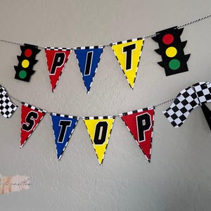 May include: A colorful banner with the words "PIT STOP" in black letters on triangular flags. The flags are red, blue, yellow, and black with a checkered pattern. There are also two black and white checkered flags and a red, yellow, and green traffic light.
