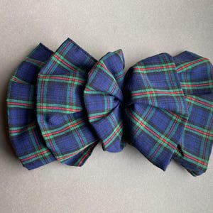 May include: A blue, green, and red plaid fabric bow. The bow is made of a soft material and has a classic plaid pattern. The bow is a decorative accessory.