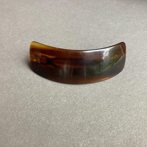 May include: A curved, tortoiseshell-patterned hair clip. The clip is a warm brown color with a glossy finish. The shape is a gentle arc, designed to hold hair securely. This accessory is suitable for various hairstyles.