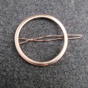 May include: A gold-toned metal hair clip with a circular design. The clip has a simple, elegant look and is perfect for holding hair in place.