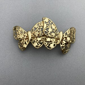 May include: Gold-toned metal butterfly hair clip with intricate cut-out details. The clip features three butterflies connected together.
