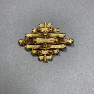 May include: A gold-toned brooch in the shape of a geometric design, resembling a stylized bamboo pattern.