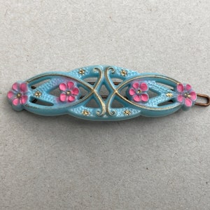 May include: A light blue hair clip with a decorative design featuring pink flowers and gold accents.