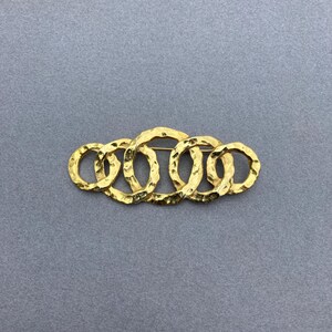 May include: A gold-toned brooch made of five interlocking, textured rings.