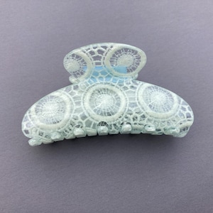 May include: A white and light blue plastic hair claw with a lace design.