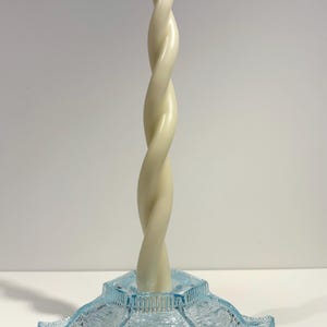 Puede incluir: Una vela blanca retorcida se asienta sobre un candelero de vidrio azul con base hexagonal.