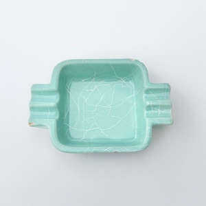 Puede incluir: Un cenicero de cerámica azul claro con un diseño de mármol blanco. El cenicero tiene una forma cuadrada con esquinas redondeadas y cuatro pequeñas hendiduras en los lados.