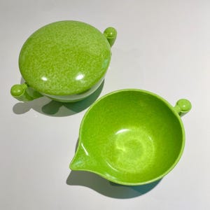May include: A green speckled ceramic sugar bowl and creamer set with two handles on the bowl and one handle on the creamer.