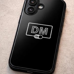Puede incluir: Funda de teléfono negra con acabado brillante. La funda presenta un diseño rectangular blanco con las letras "DM" y la palabra "ON" debajo. La funda del teléfono tiene un recorte para la cámara.