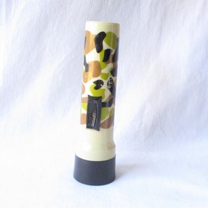 May include: A camouflage patterned flashlight with a black end cap. The flashlight is made of plastic and has a white body with black, green, and brown camouflage patterns.