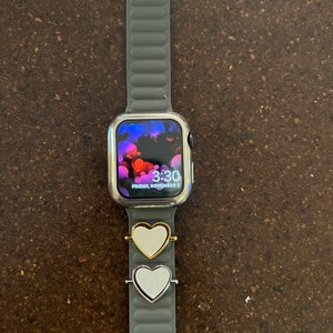 May include: A silver Apple Watch with a gray silicone band and a white heart charm. The watch face displays the time 3:30 and the date Friday, November 3.
