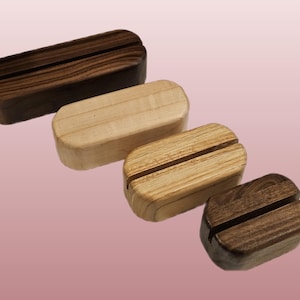 May include: Four rectangular wooden display stands with rounded corners and a centered slot along the top. The stands vary in size and wood grain color, ranging from a dark brown walnut tone to a lighter, natural beige wood finish.