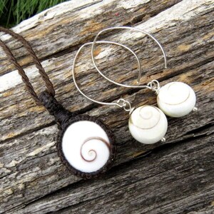 May include: A set of shell jewelry featuring a brown cord necklace with a white shell pendant and a pair of silver earrings with white shell drops.