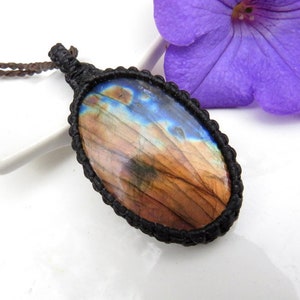 May include: A brown and blue labradorite gemstone pendant with a black cord necklace. The gemstone is oval shaped and has a natural, iridescent finish.
