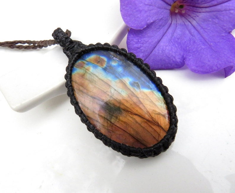 May include: A brown and blue labradorite gemstone pendant with a black cord necklace. The gemstone is oval shaped and has a natural, iridescent finish.