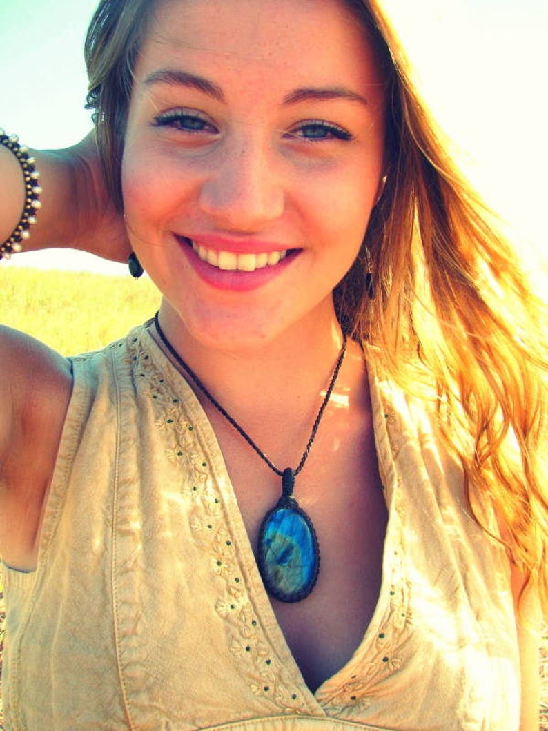 May include: A woman with long blonde hair is wearing a light brown sleeveless top with a blue and green gemstone pendant necklace.