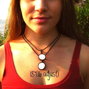 May include: A black cord necklace with two white pendant charms. The necklace is 18 inches long and can be adjusted to 16 inches. The charms are round and have a swirl design.