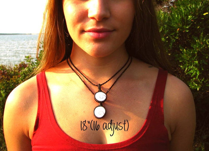 May include: A black cord necklace with two white pendant charms. The necklace is 18 inches long and can be adjusted to 16 inches. The charms are round and have a swirl design.