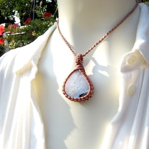 Pode incluir: Um pingente de pedra branca com um colar de cordão rosa. O pingente é envolto em um estilo macramê com um cordão rosa.